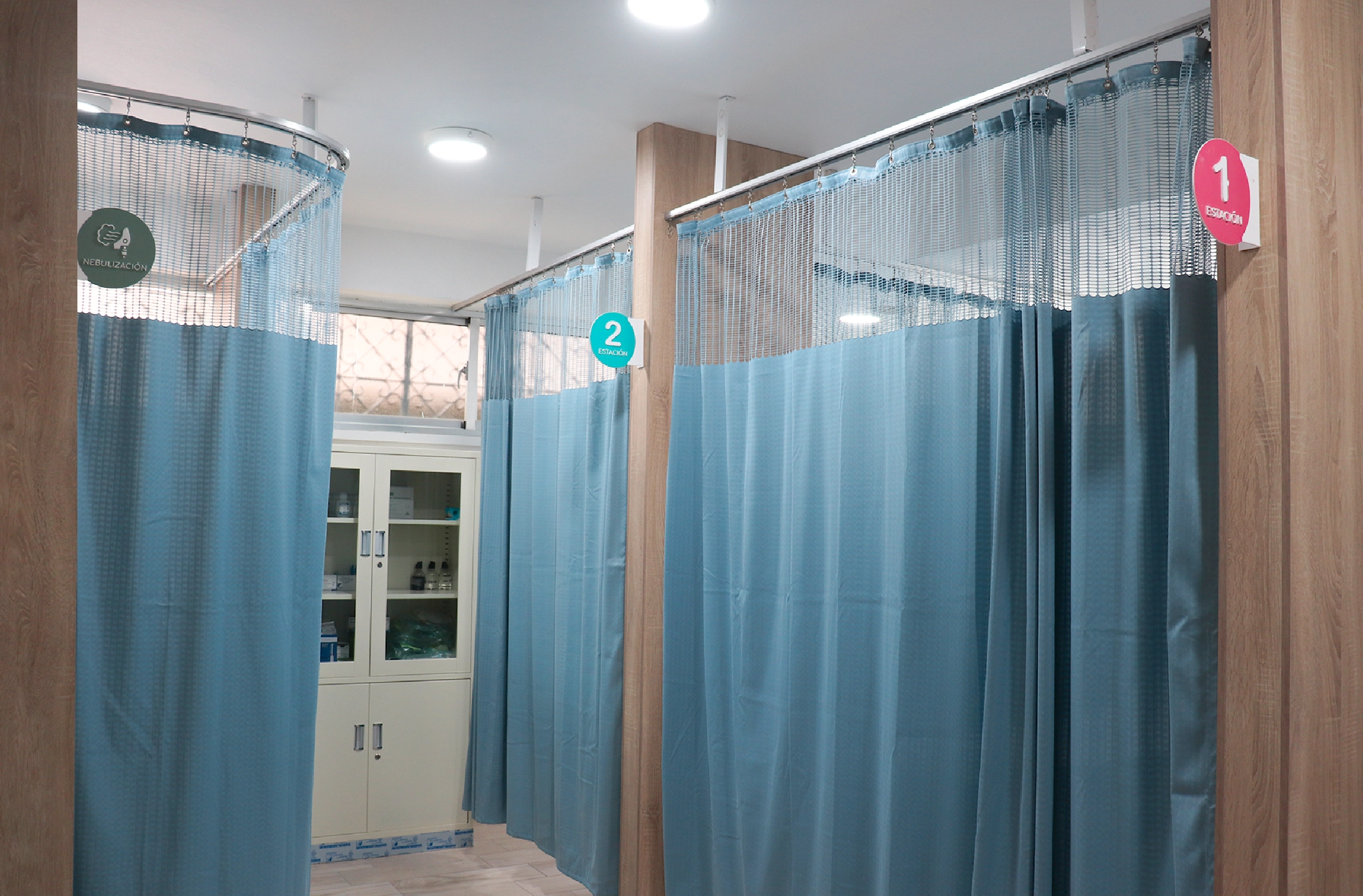 Medical cubicles with light blue privacy curtains numbered 1 and 2 inside a clinical treatment room.