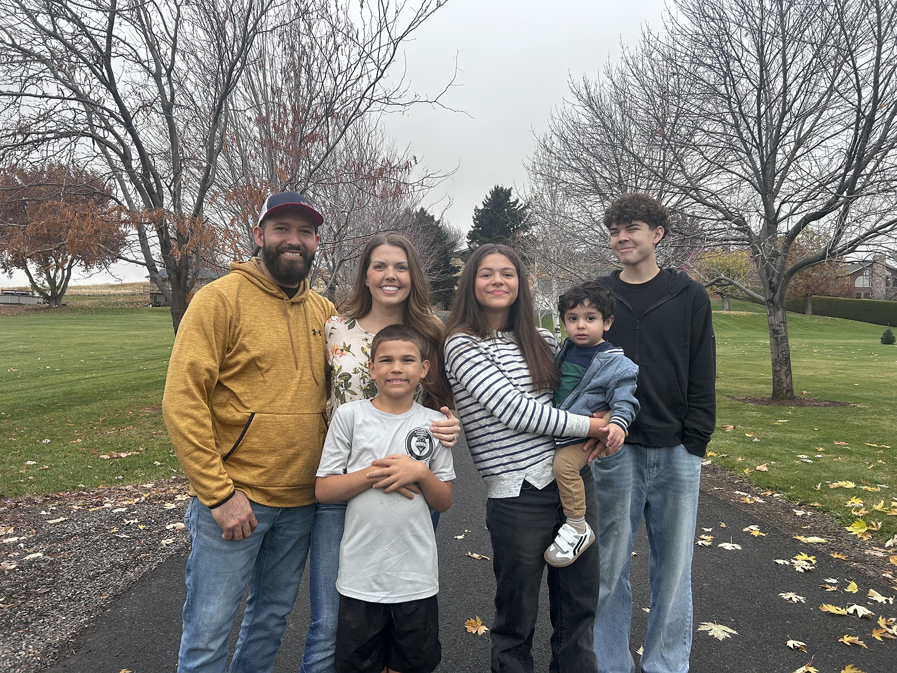 Luna family of six standing on a paved path with autumn trees and green grass in the background.