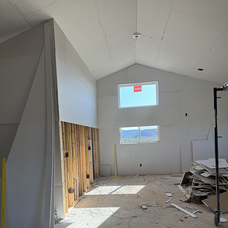 Interior of a room under construction with drywall partially installed and two windows showing a mountain view.