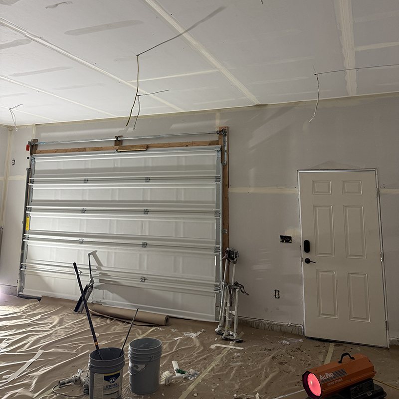 Garage interior under renovation with a partially installed garage door, painting supplies, and a portable heater.