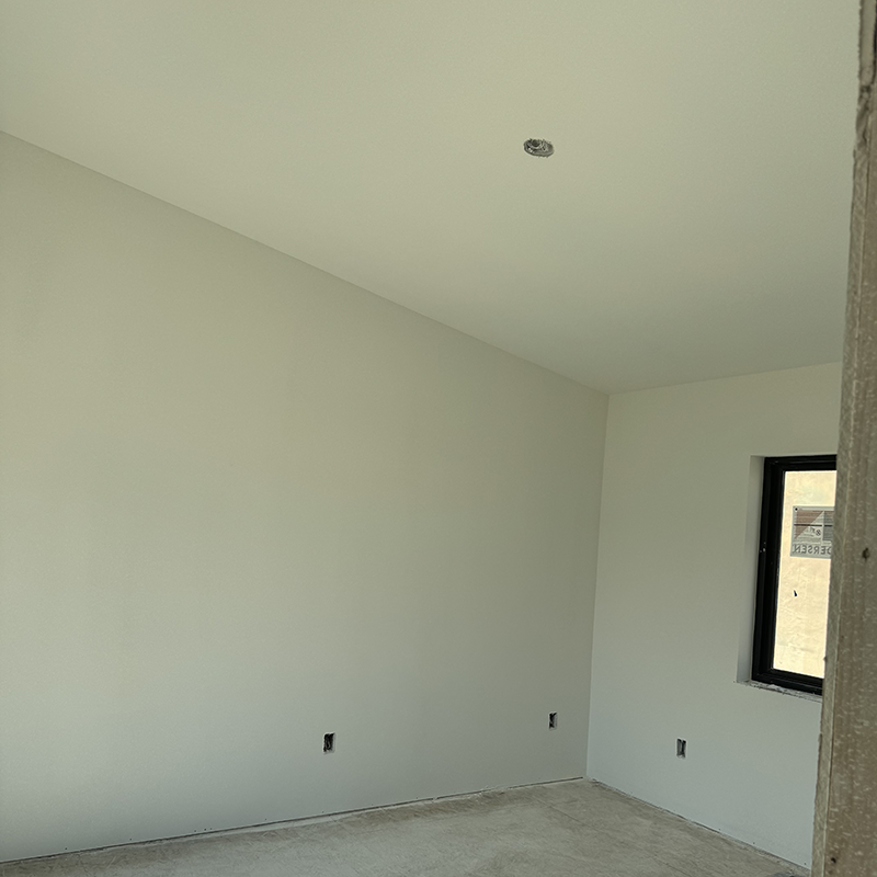 Empty room with light gray walls, unfinished concrete floor, and a small window with black frame.