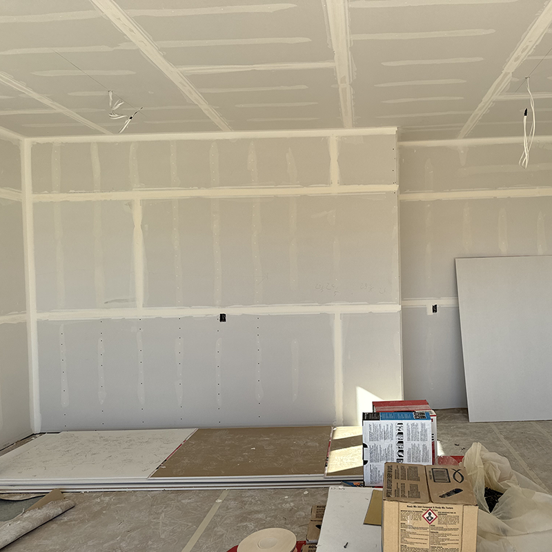 Interior of a room under construction with drywall installed and stacked construction materials on the floor.
