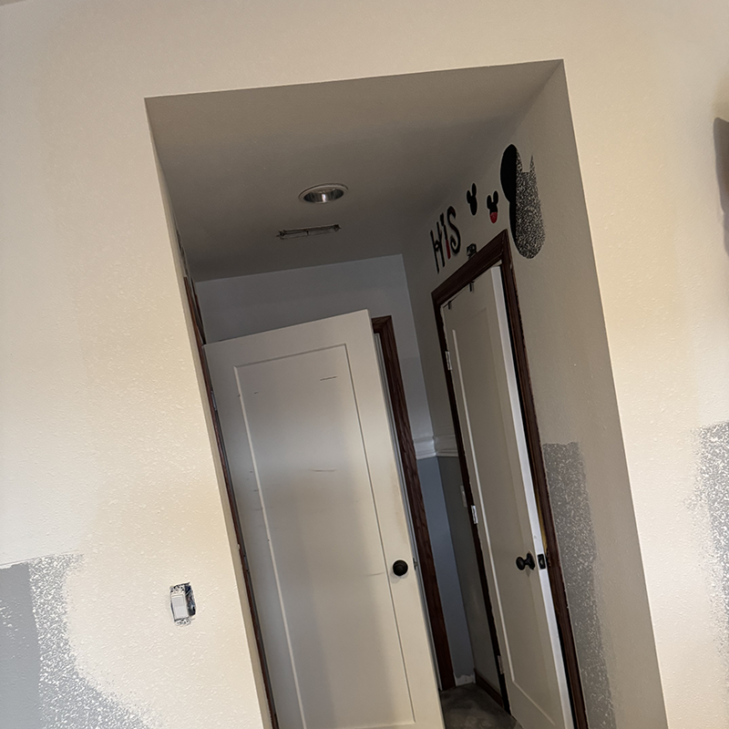 Two white doors in a hallway with beige walls, one door slightly open and the word 'HIS' with Mickey Mouse shapes on the wall above the right door.