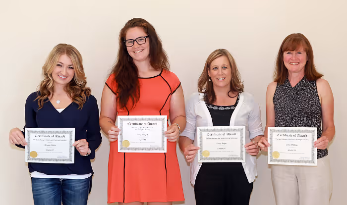 Four women standing side by side holding certificates of award and smiling.