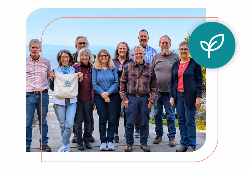 Group of ten adults standing outdoors on a paved path with mountains in the background, one woman holding a white tote bag with a blue and yellow logo.