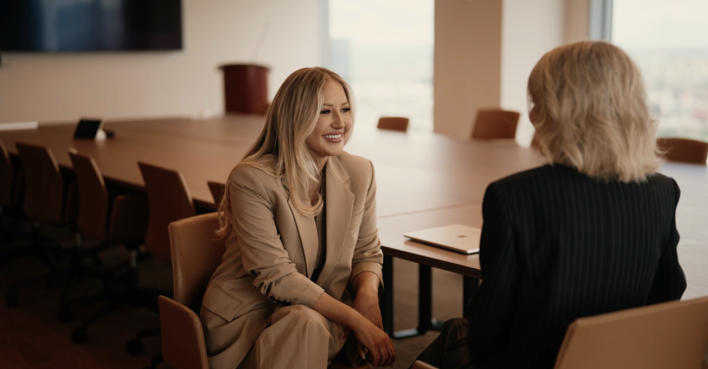 Two women talking in a boardroom beside large windows