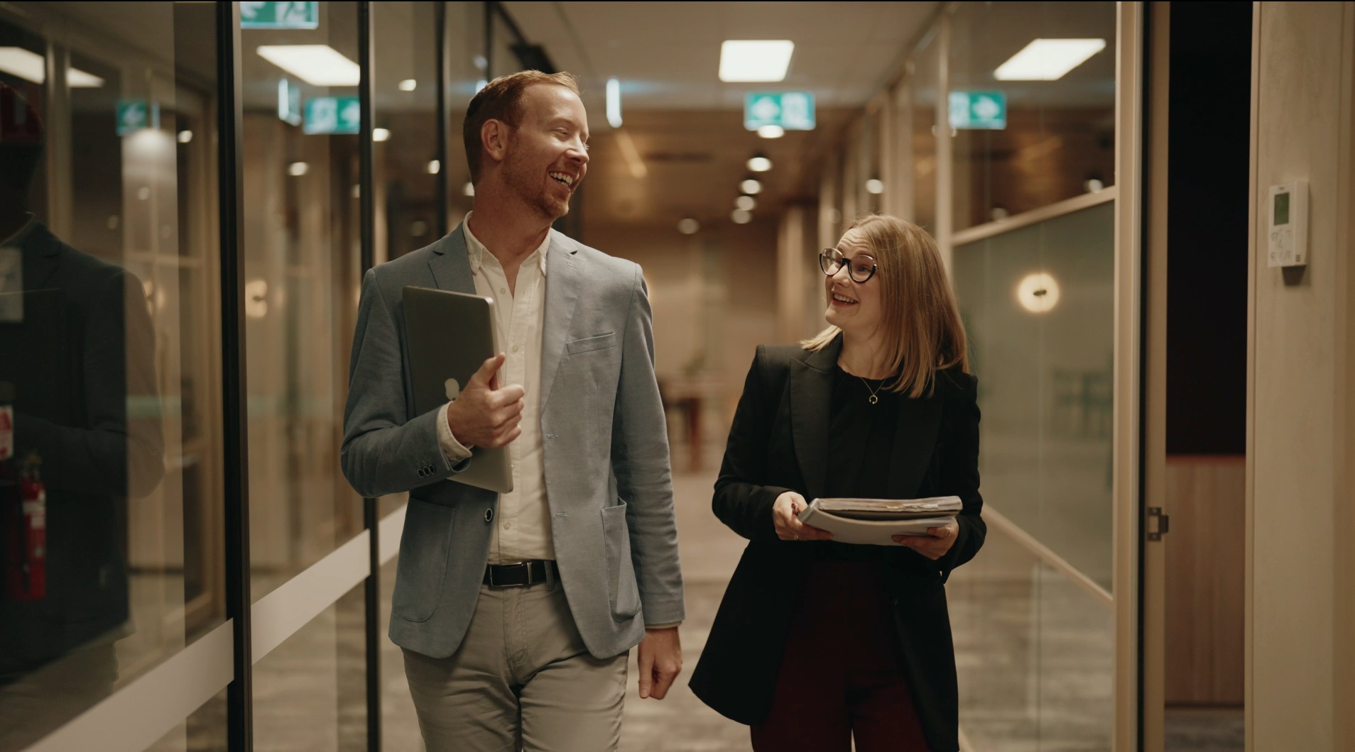 Two colleagues chatting while walking through an office corridor