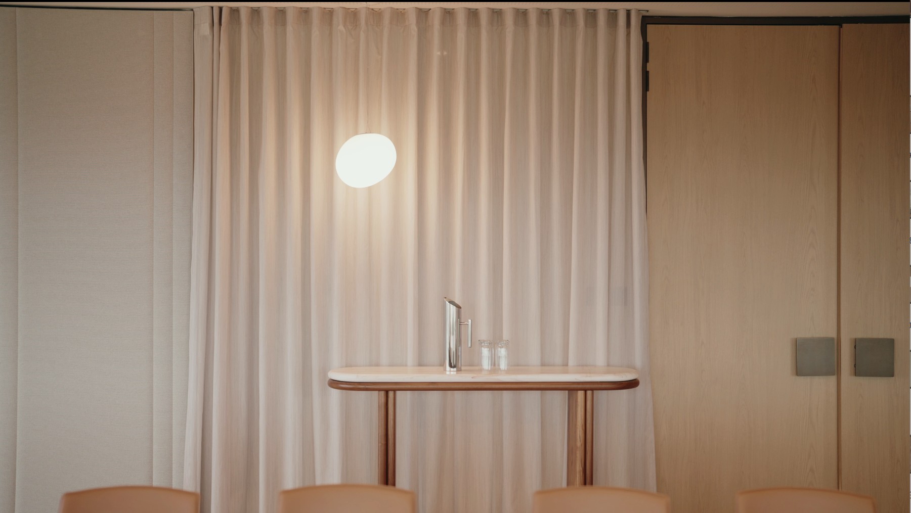Small table with water carafe and glasses in front of a curtained wall
