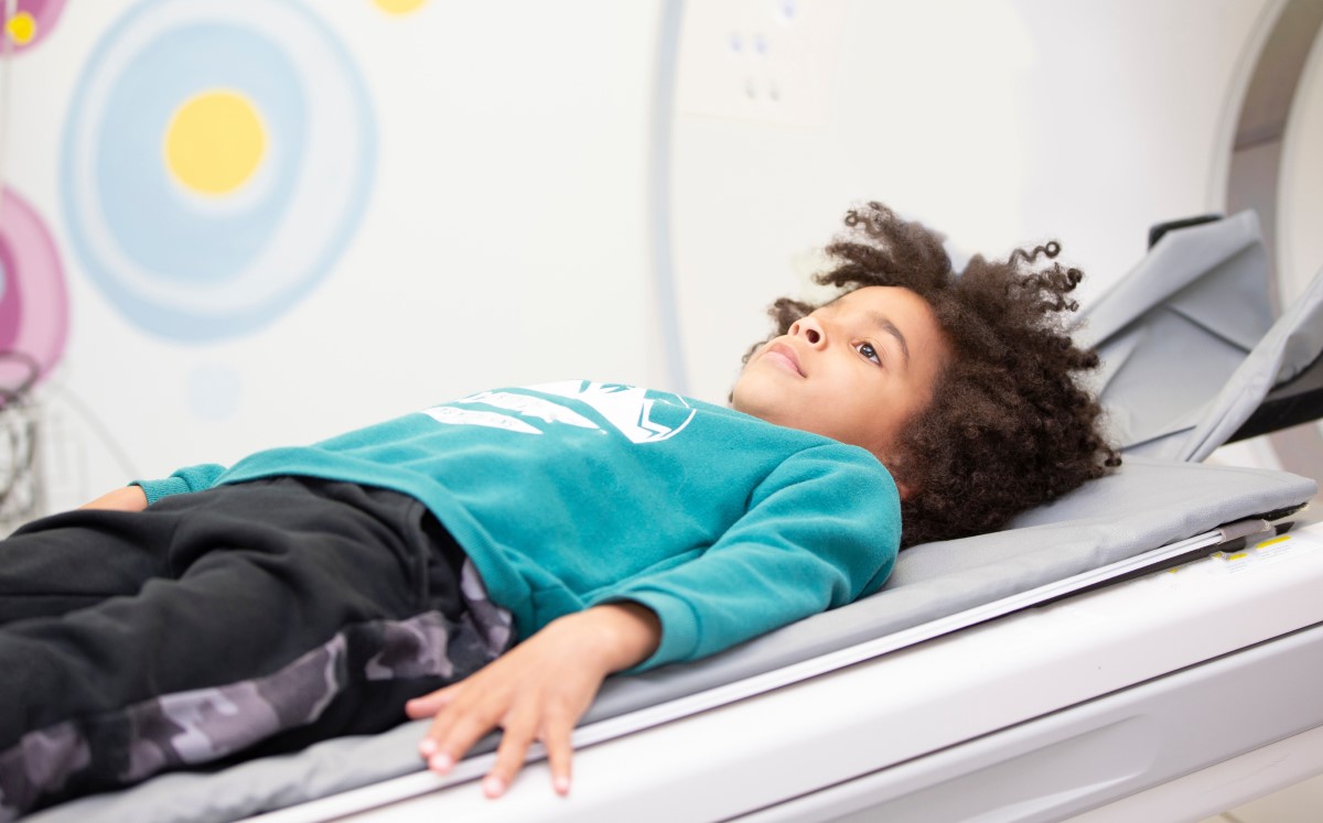 Child with curly hair lying on a padded medical exam table, looking upward.