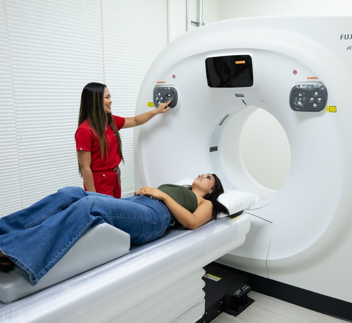 Technician in red scrubs preparing a patient lying on a CT scan machine bed for a scan.