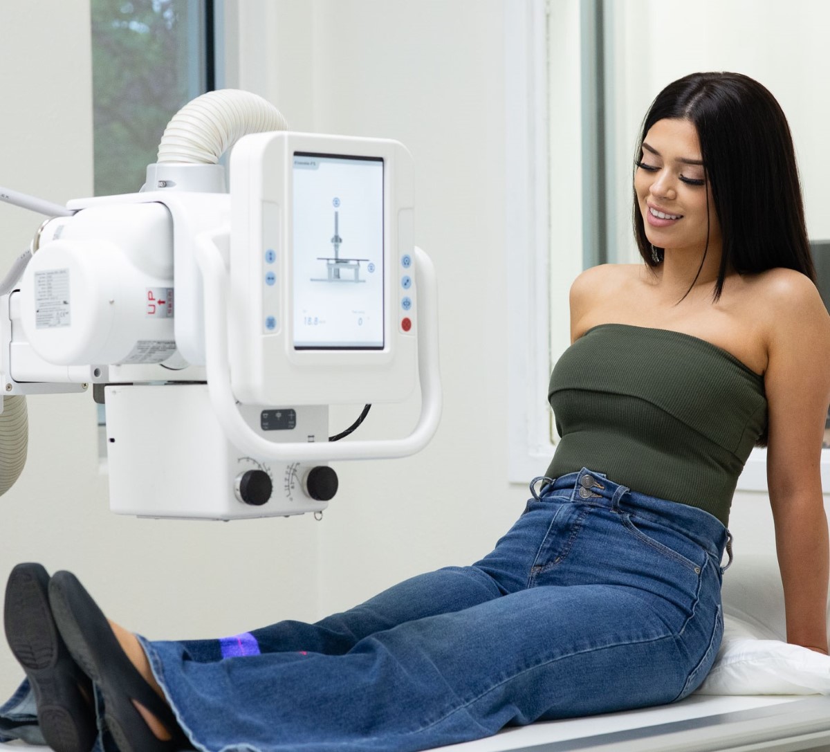 Patient sitting on a medical examination bed near a Digital X-ray machine.