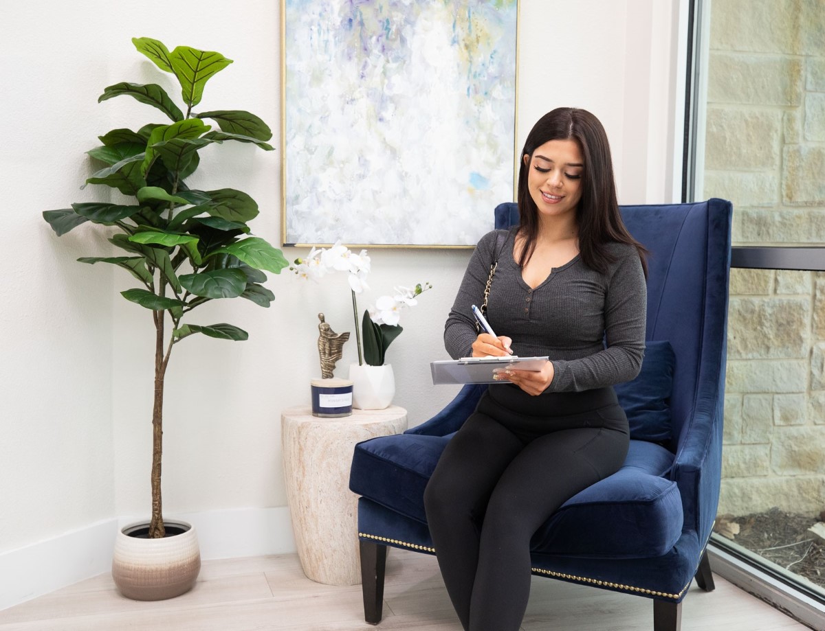 Young woman sitting in the Open MRI waiting room writing on a clipboard