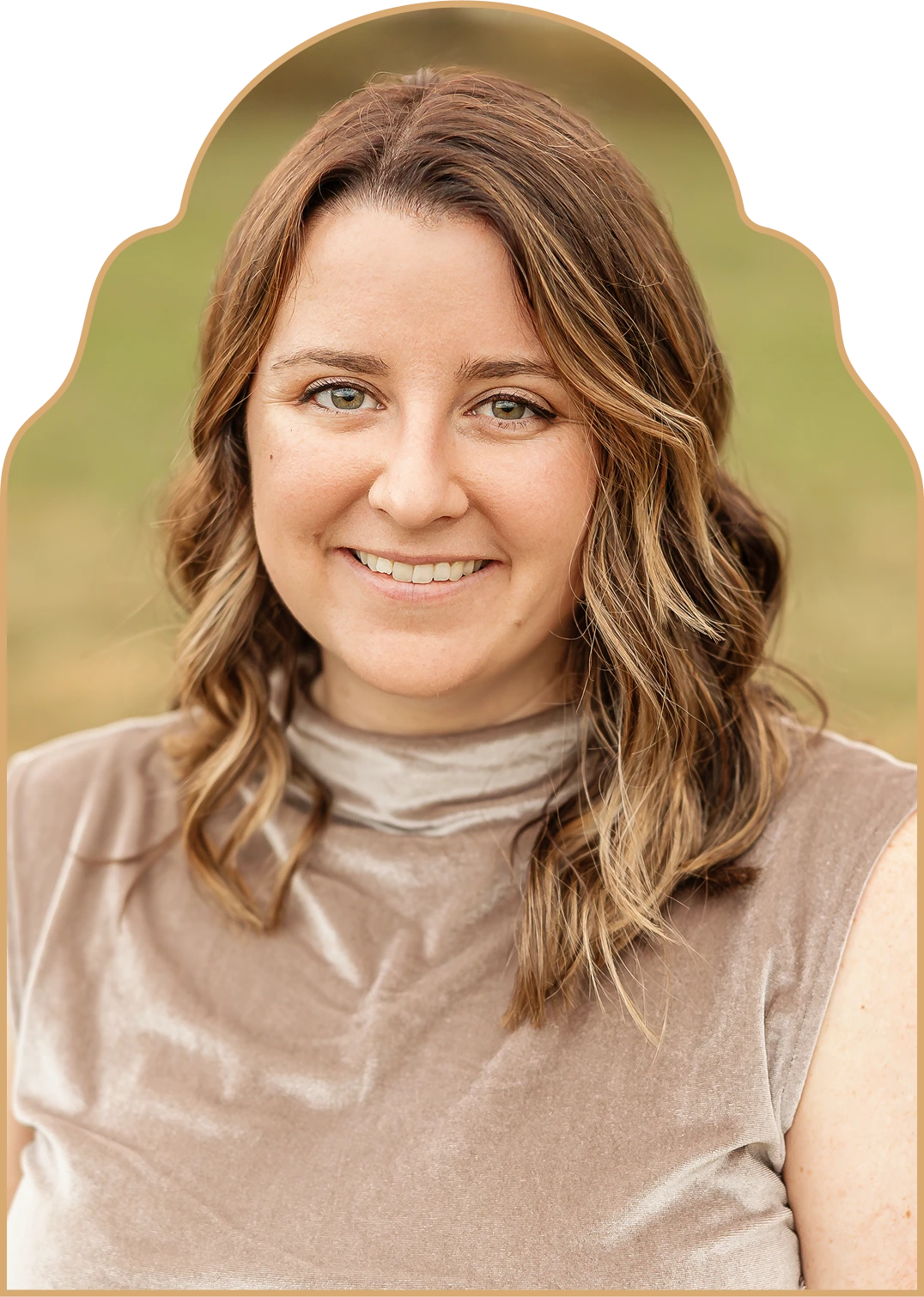 Rebecca Cooney with shoulder-length wavy brown hair and green eyes wearing a beige sleeveless top outdoors.