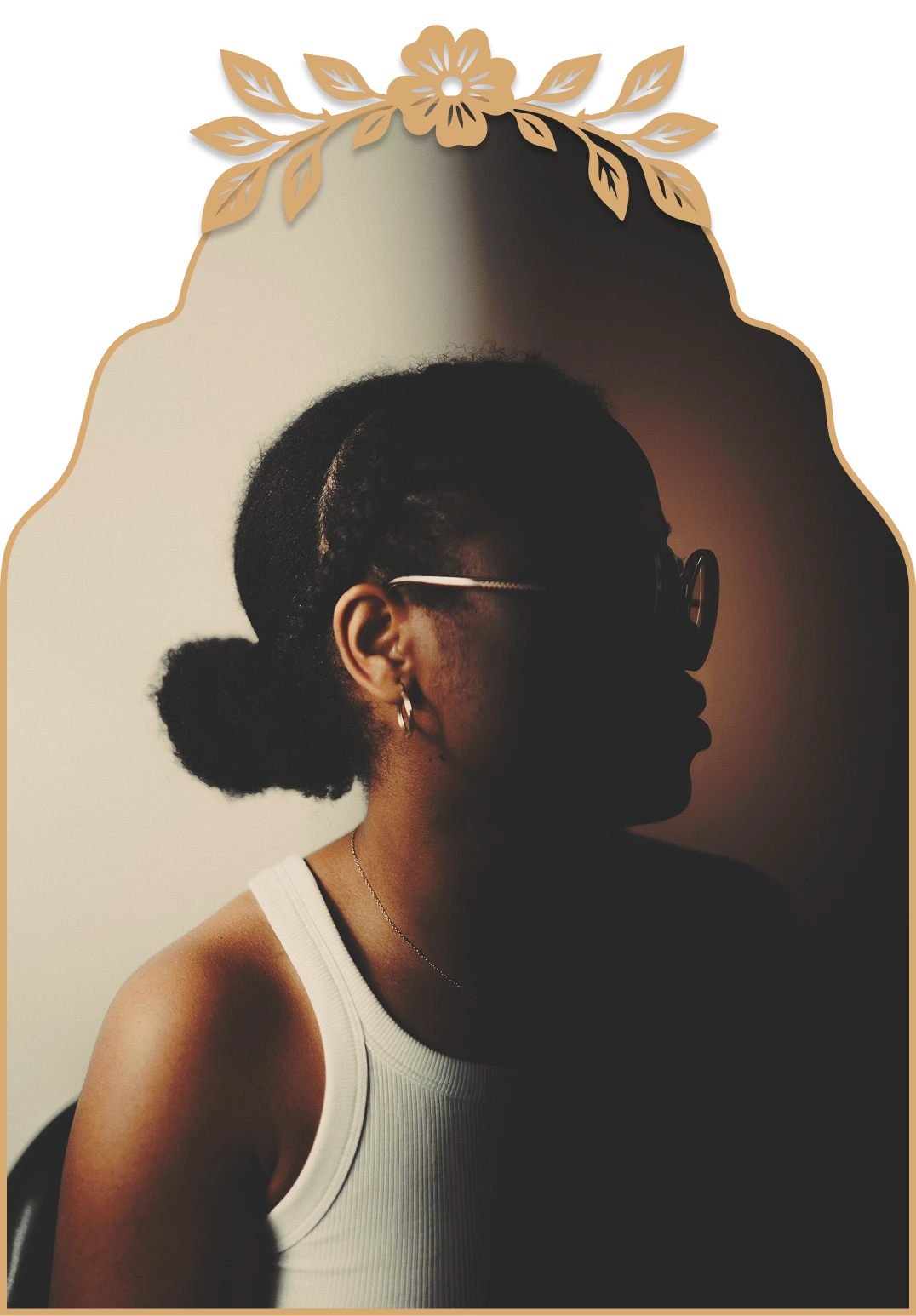 Side profile of a person with braided hair in a bun wearing glasses, hoop earrings, and a white tank top, with dramatic lighting casting half the face in shadow.