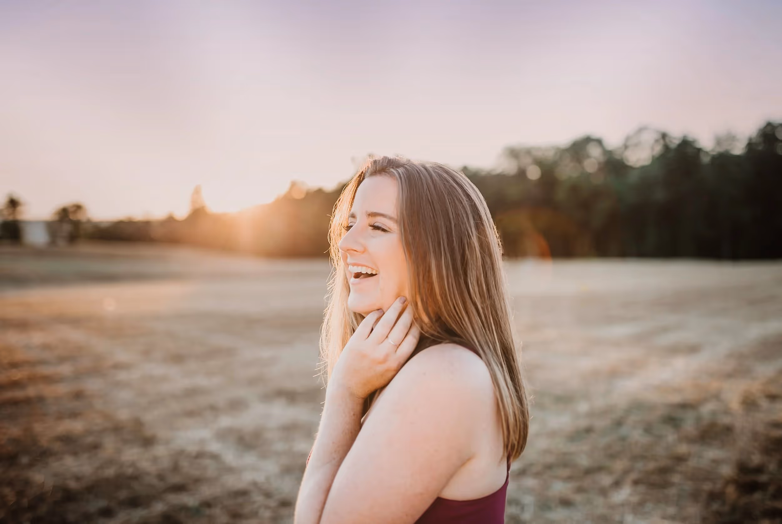 Woman with long hair laughing outdoors at sunset in a field.