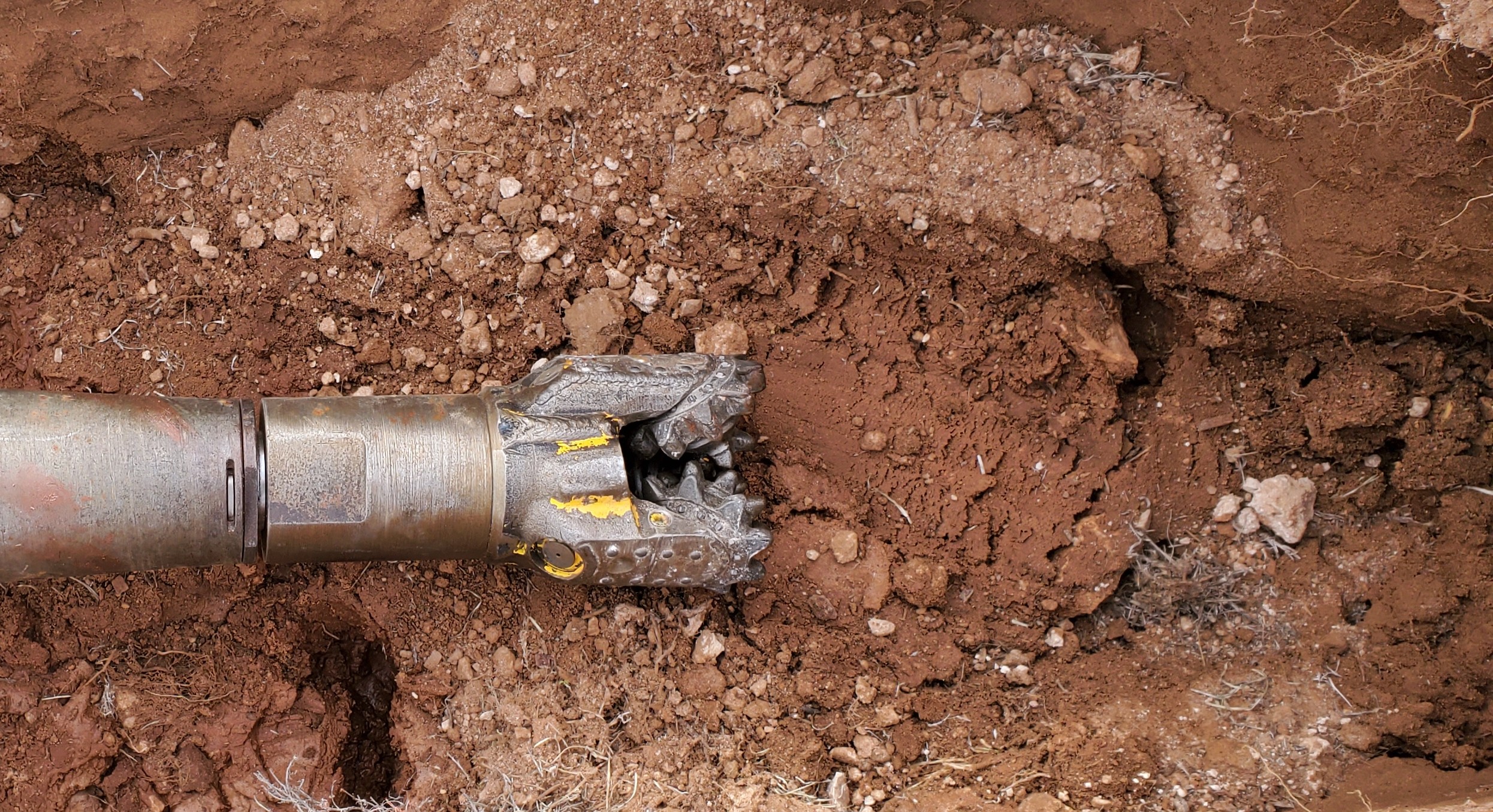 Metal drilling tool cutting through dry, rocky soil during excavation.