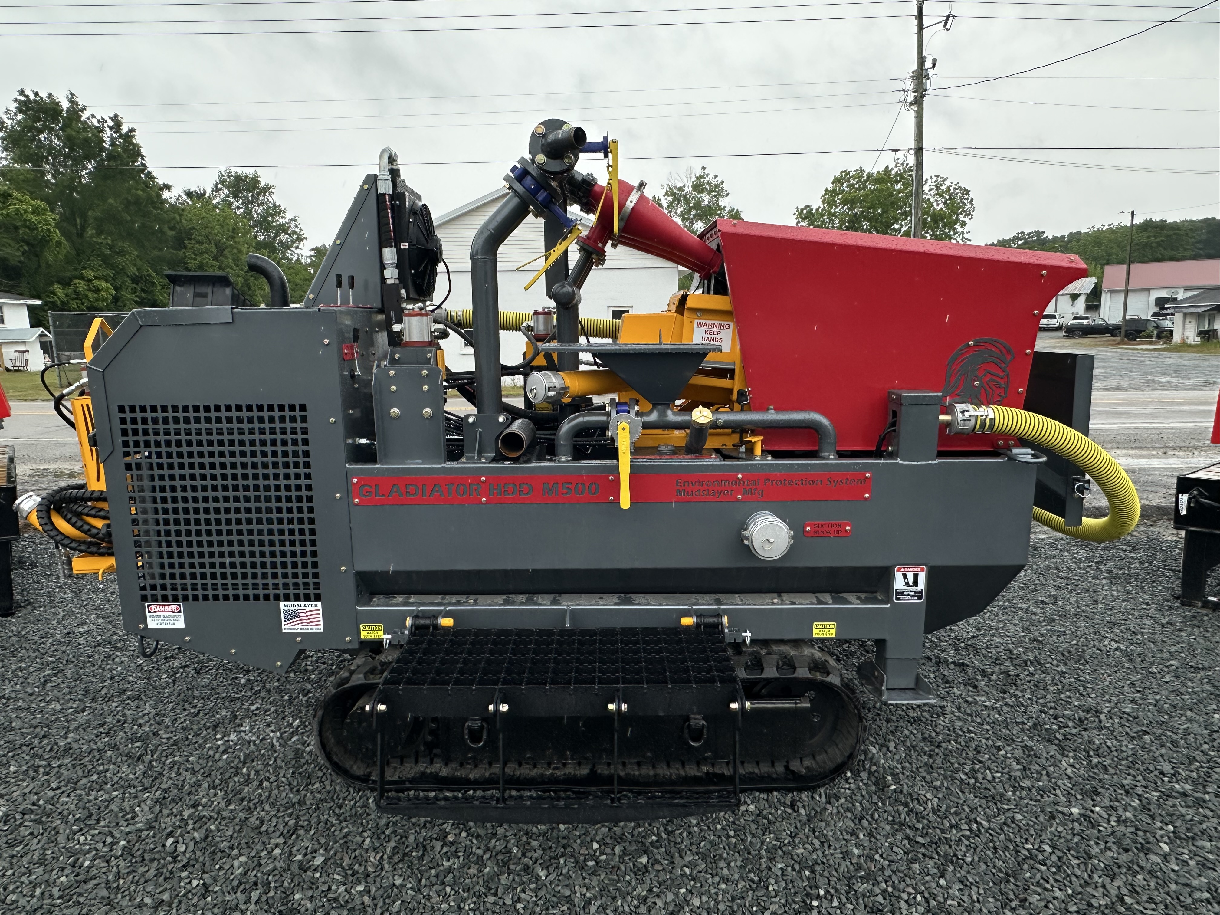 Gladiator HDD M500 mud mixing machine with red hopper and rubber tracks on gravel surface.