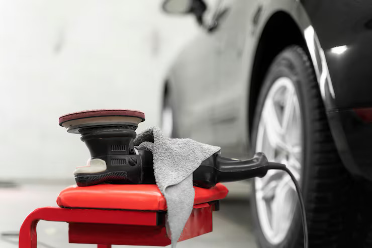 Car polishing machine with a gray cloth placed on a red stool beside a black car tire.