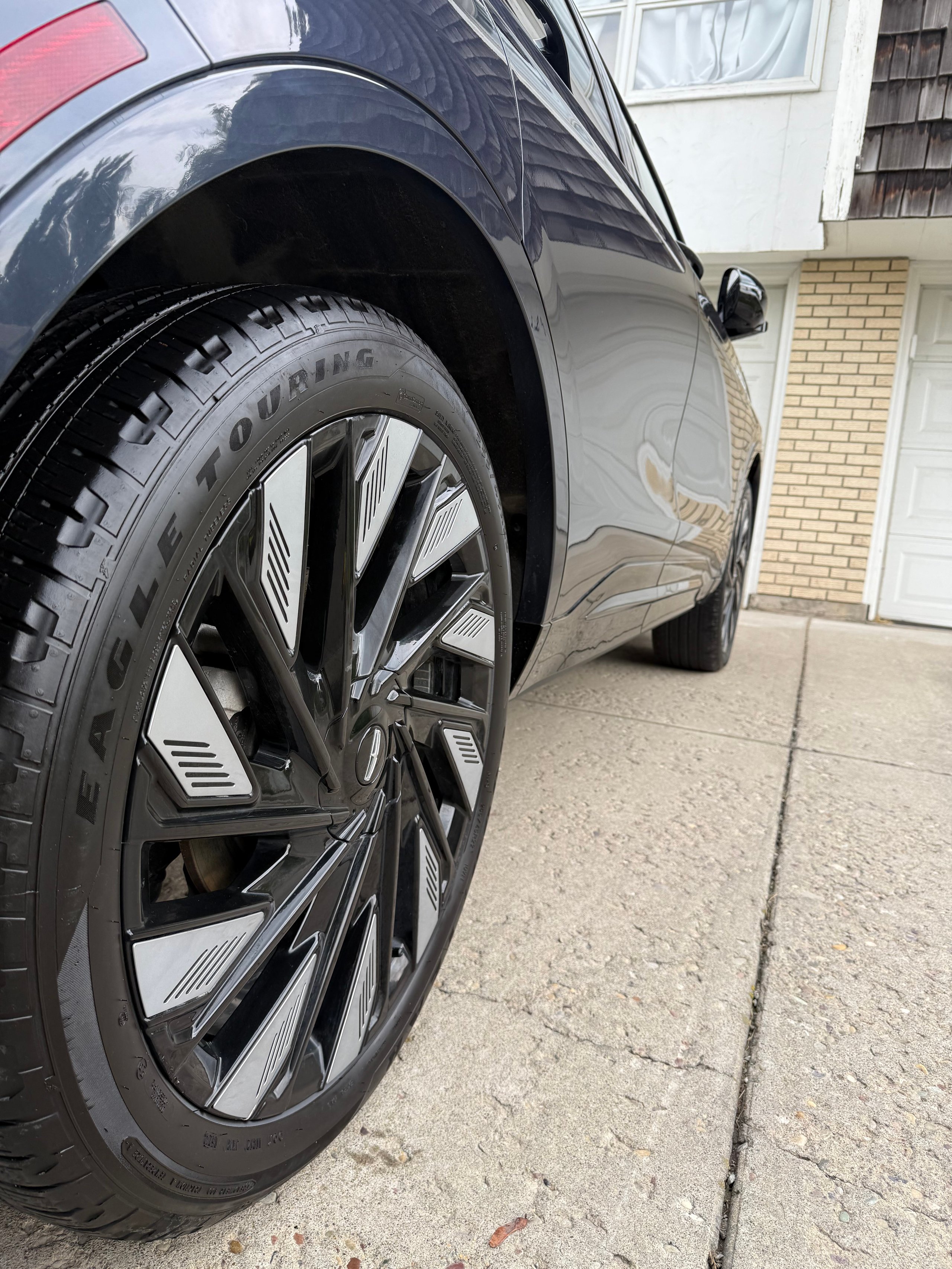 Close-up of a black and silver car wheel with Eagle Touring tire on a concrete driveway in front of a garage.