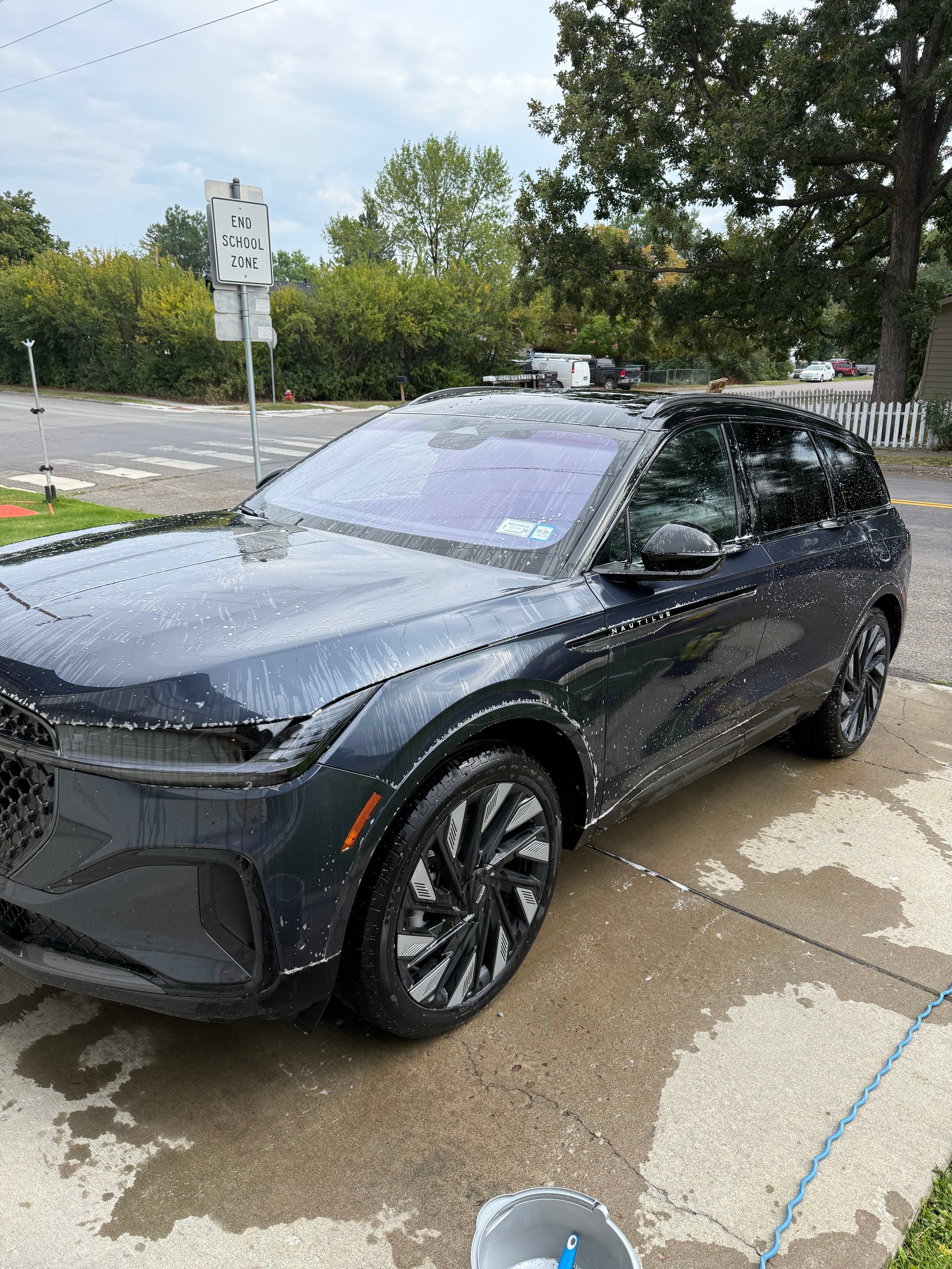 Dark blue Lincoln Nautilus SUV being washed with water and soap on a driveway.