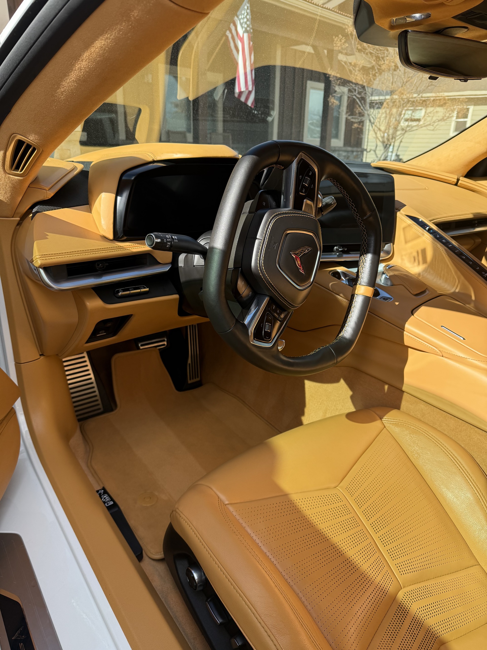 Interior of a car with tan leather seats, a black leather steering wheel displaying a Corvette emblem, and a digital dashboard.