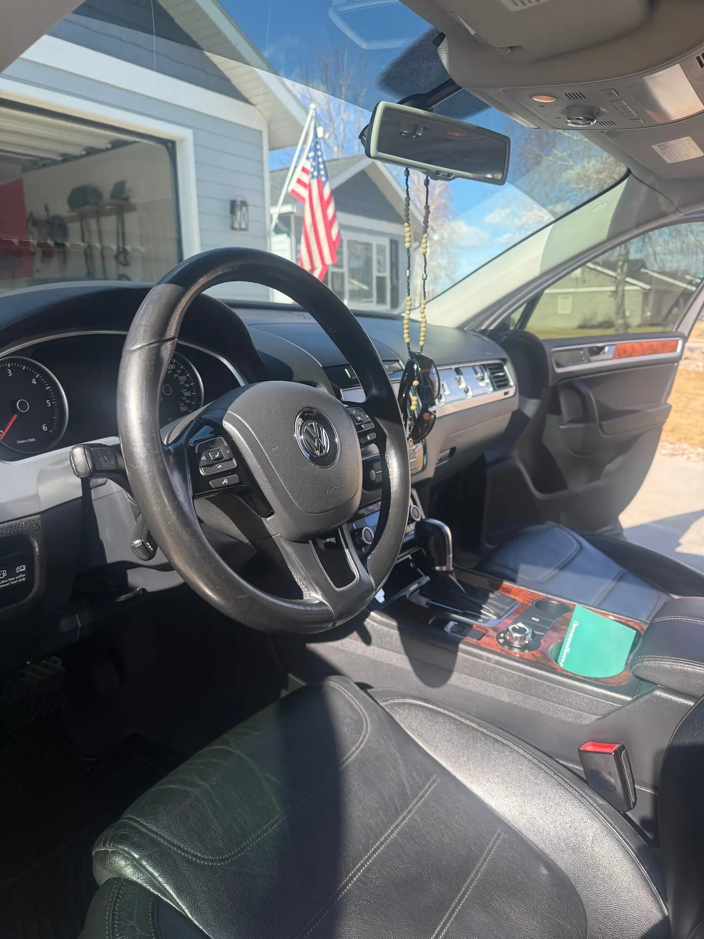 Interior view of a Volkswagen car showing a leather steering wheel, dashboard, black leather seats, and an American flag visible outside through the window.