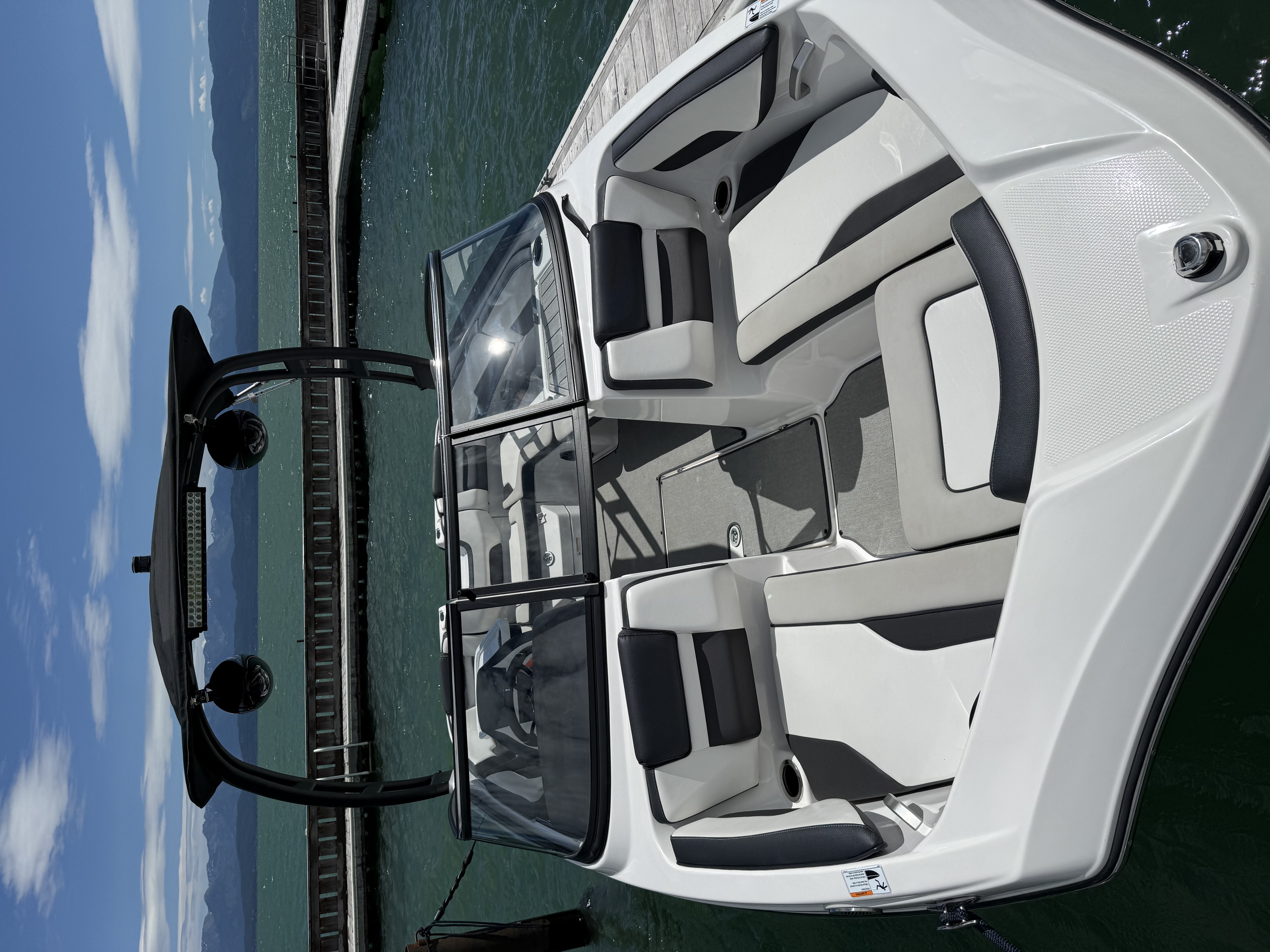 White and gray motorboat docked on clear green water with mountains and partly cloudy sky in background.