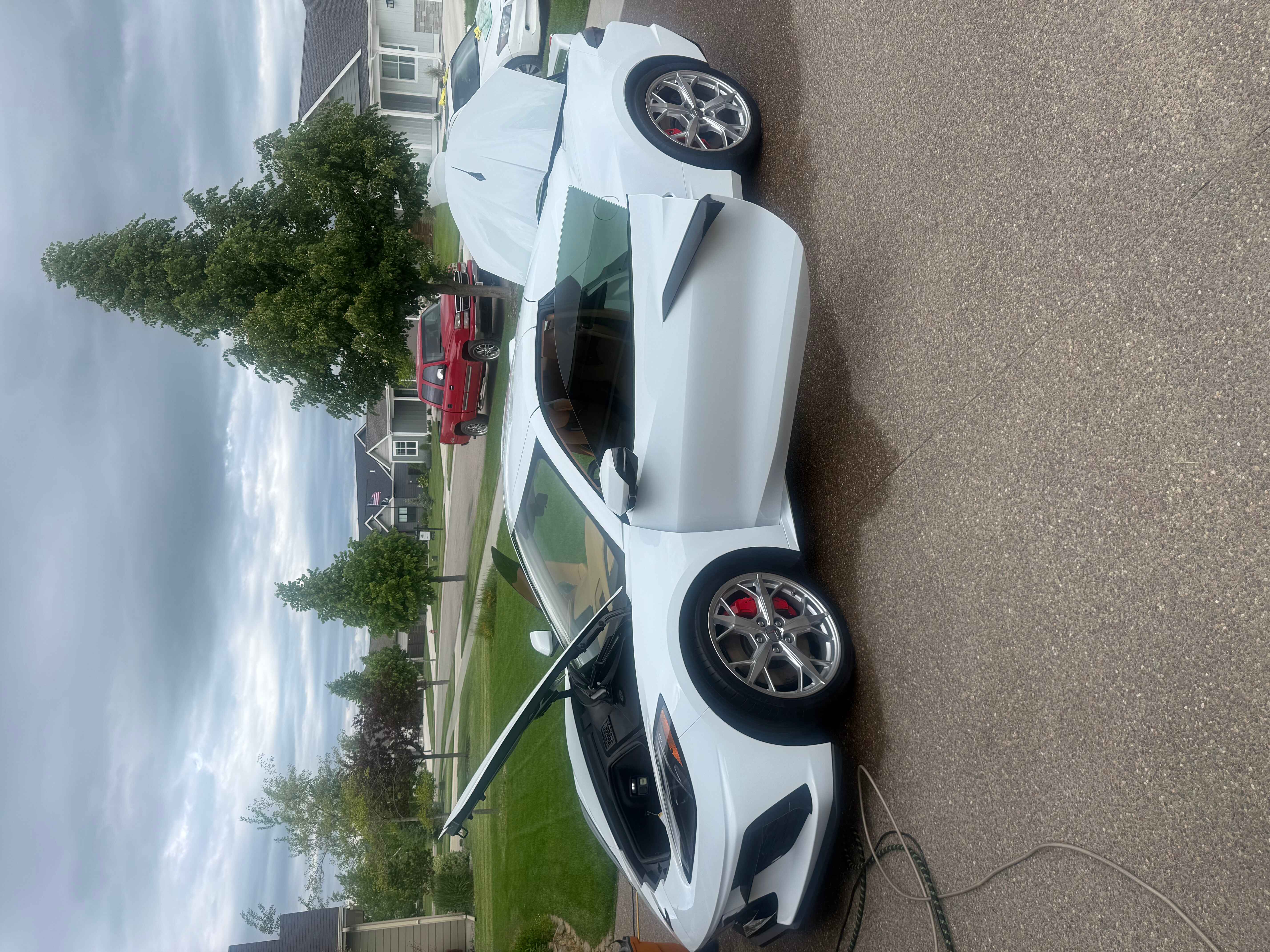 White sports car with red brake calipers parked on a driveway with the driver's door open.