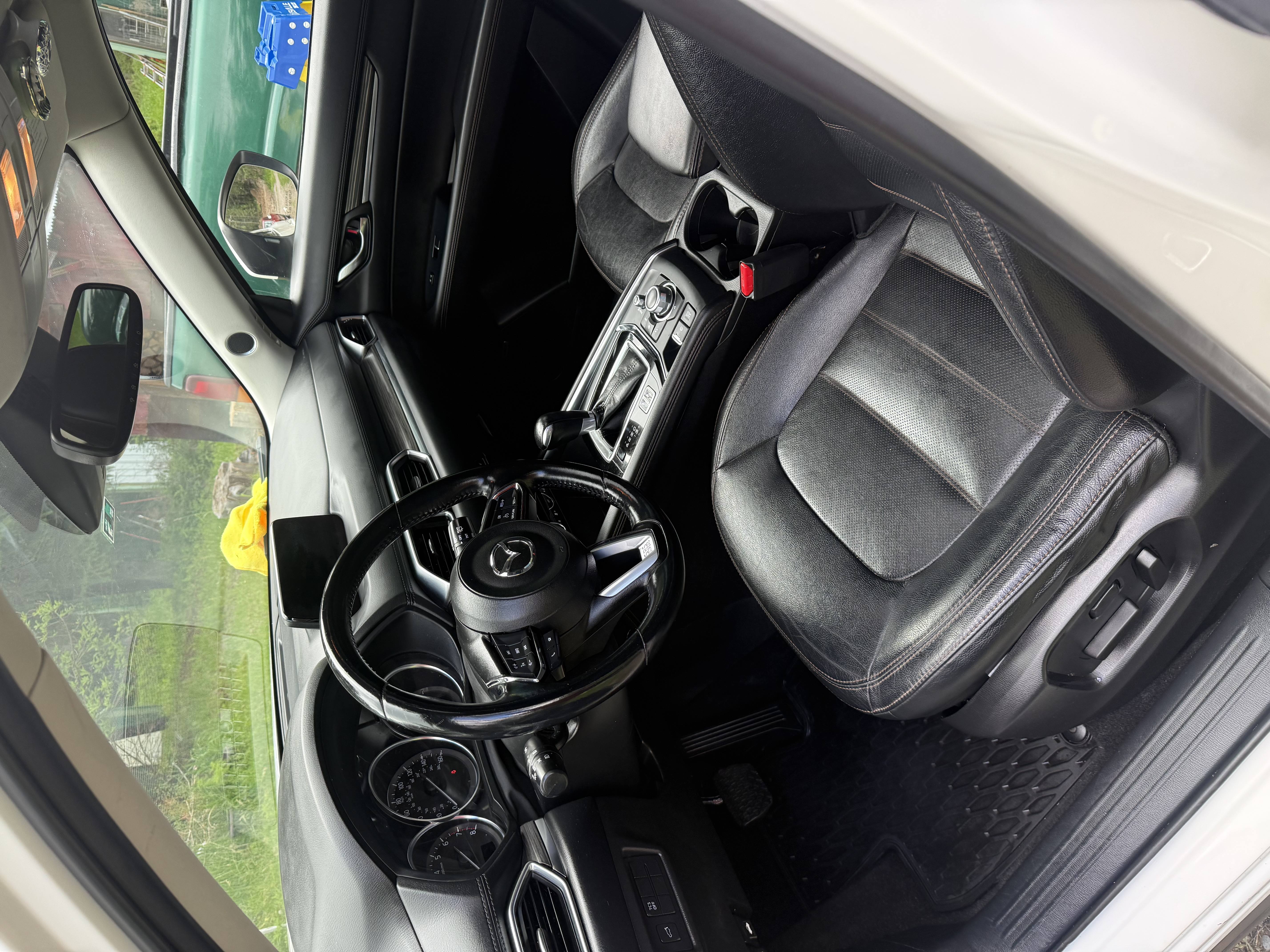 Interior of a Mazda car showing black leather driver's seat, steering wheel, and dashboard with controls.