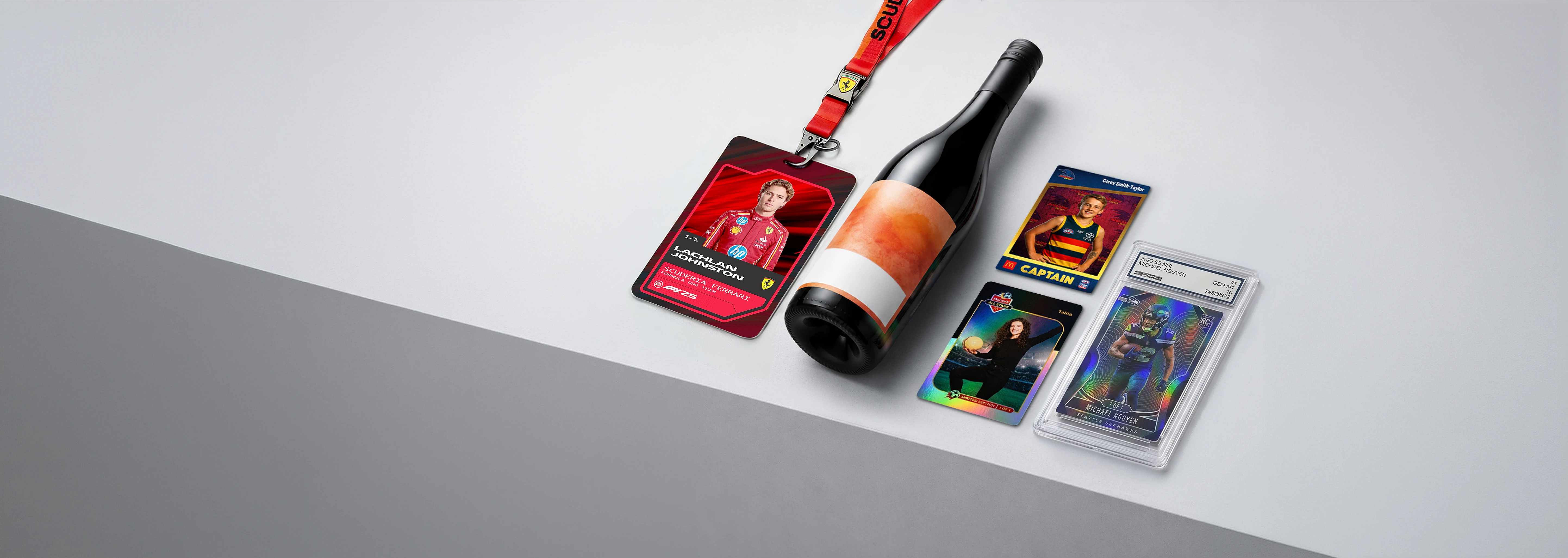 Red Ferrari event badge, bottle of wine, and three sports trading cards on a light gray surface.