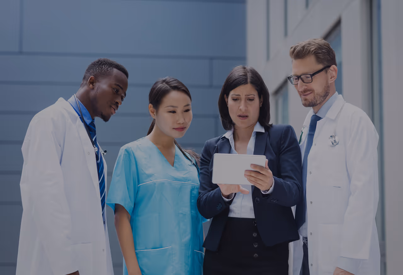 Two doctors and a nurse attentively looking at a tablet held by a businesswoman in professional attire.