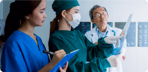 Three healthcare professionals examining medical X-ray images in a clinical setting.
