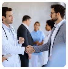 Doctor and businessman shaking hands in a medical environment with medical staff talking in the background.
