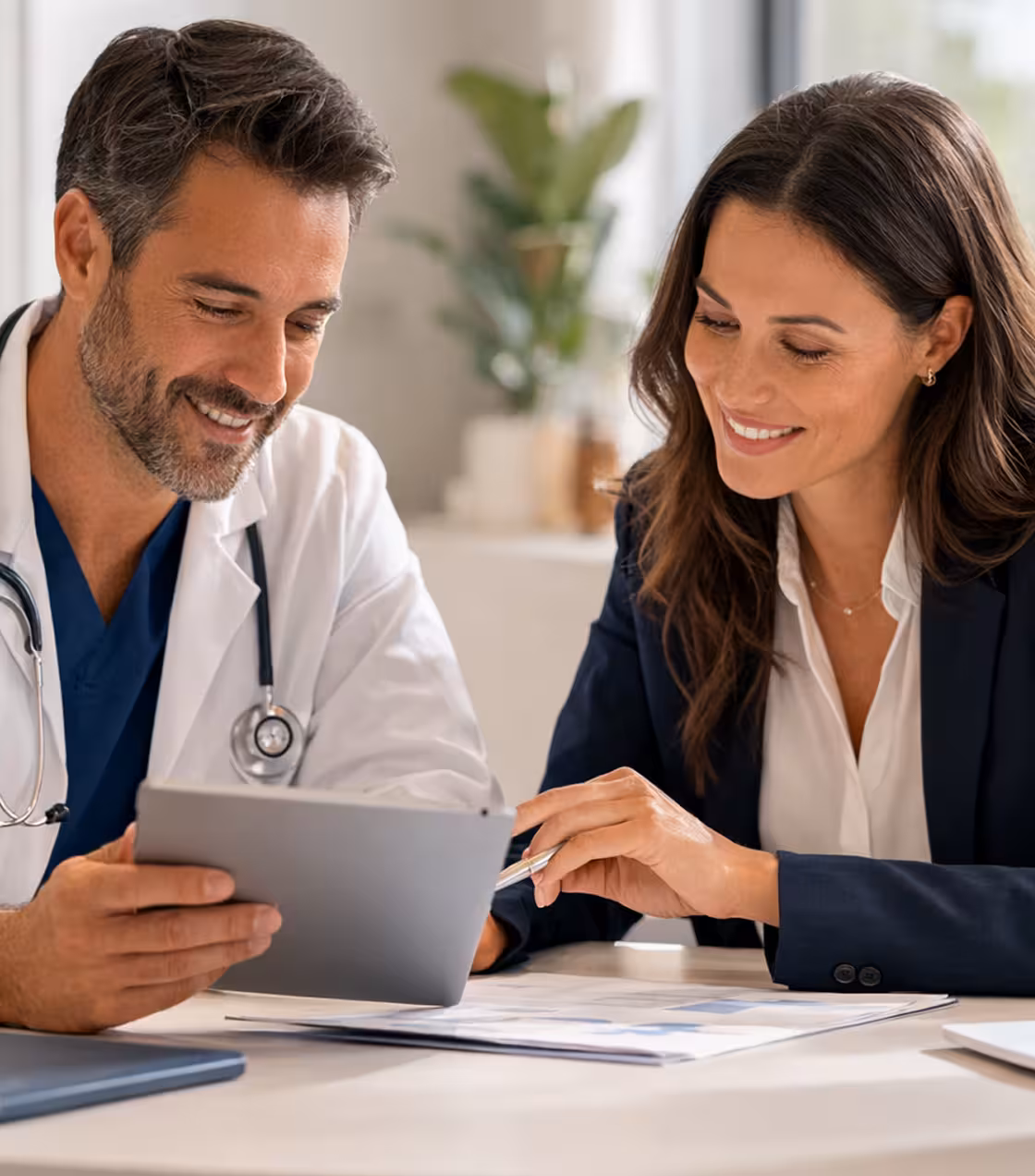 Male doctor and female patient smiling while reviewing a tablet together at a desk.