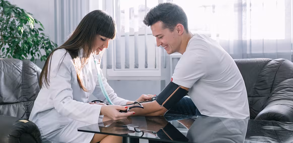Healthcare professional measuring a smiling young man's blood pressure in a bright room.