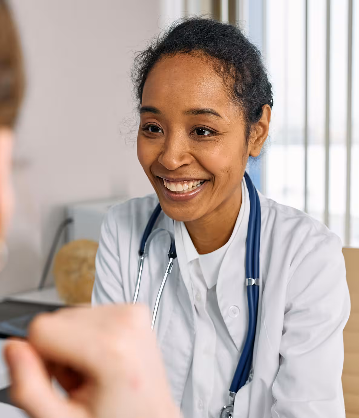Smiling female doctor wearing a white coat and stethoscope talking to a patient.