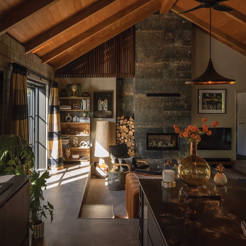 Living room at the Smith House in Greytown with vaulted timber ceiling, stone fireplace, large windows, and dark marble kitchen island.