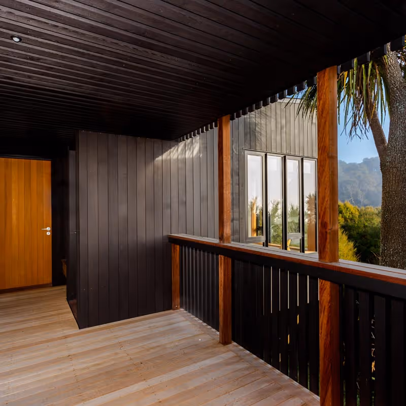 Front entrance and covered balcony at Glenmorven Studios with timber panelling and views of native bush and hills.