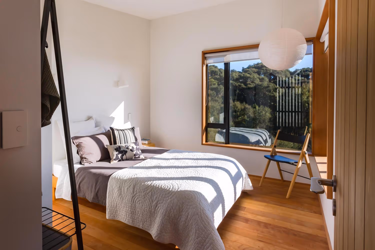 Sunlit bedroom in Glenmorven Studios, Greytown, featuring timber floors and a window with forest view.