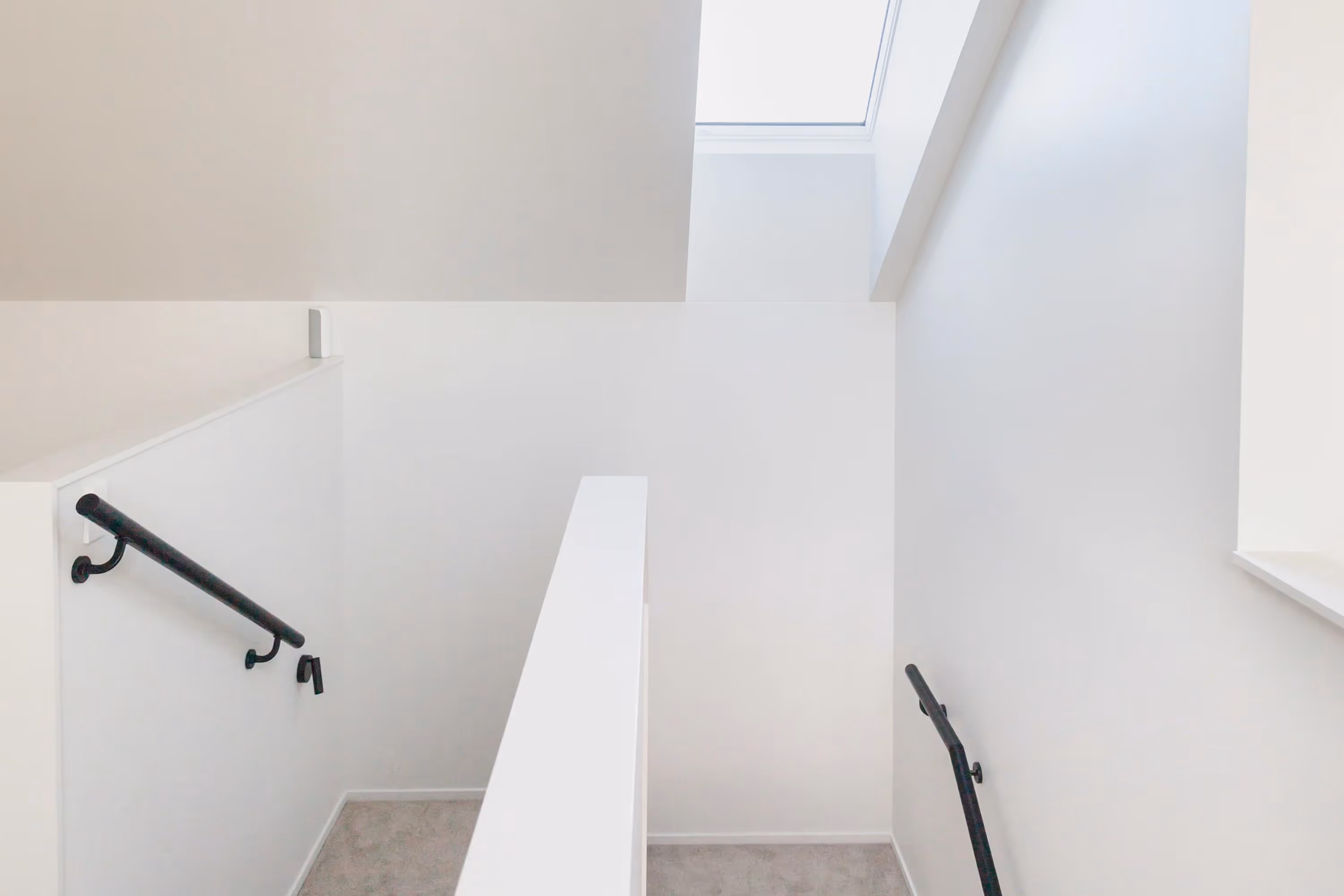 Minimalist staircase at the Saunders Residence in Greytown with white steps, black handrails, and skylight above.