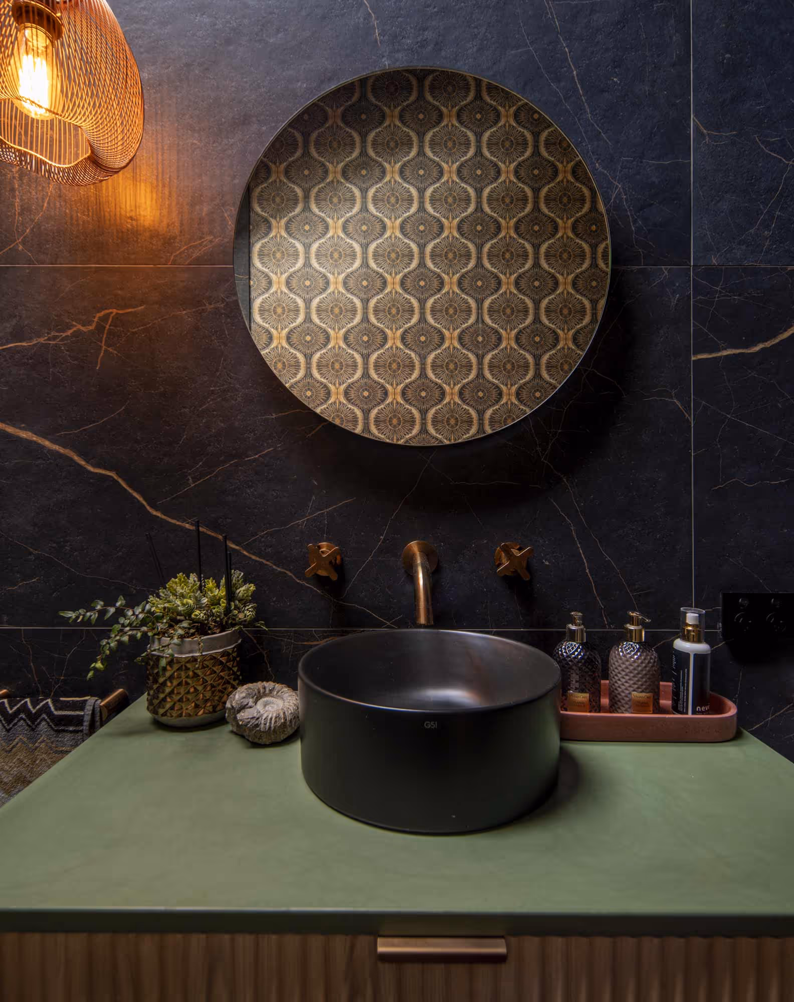 Smith House bathroom vanity with black sink, gold faucet, patterned mirror, and marble wall.