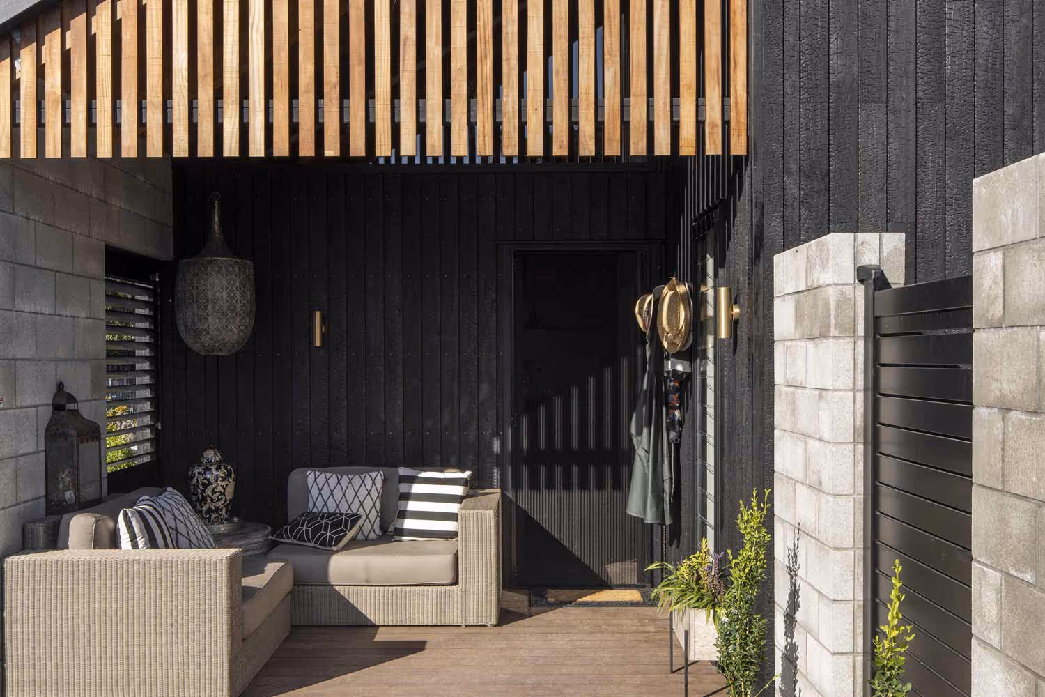 Covered outdoor patio at the Smith House in Greytown with beige wicker sofa, timber-paneled wall, and concrete pillars.
