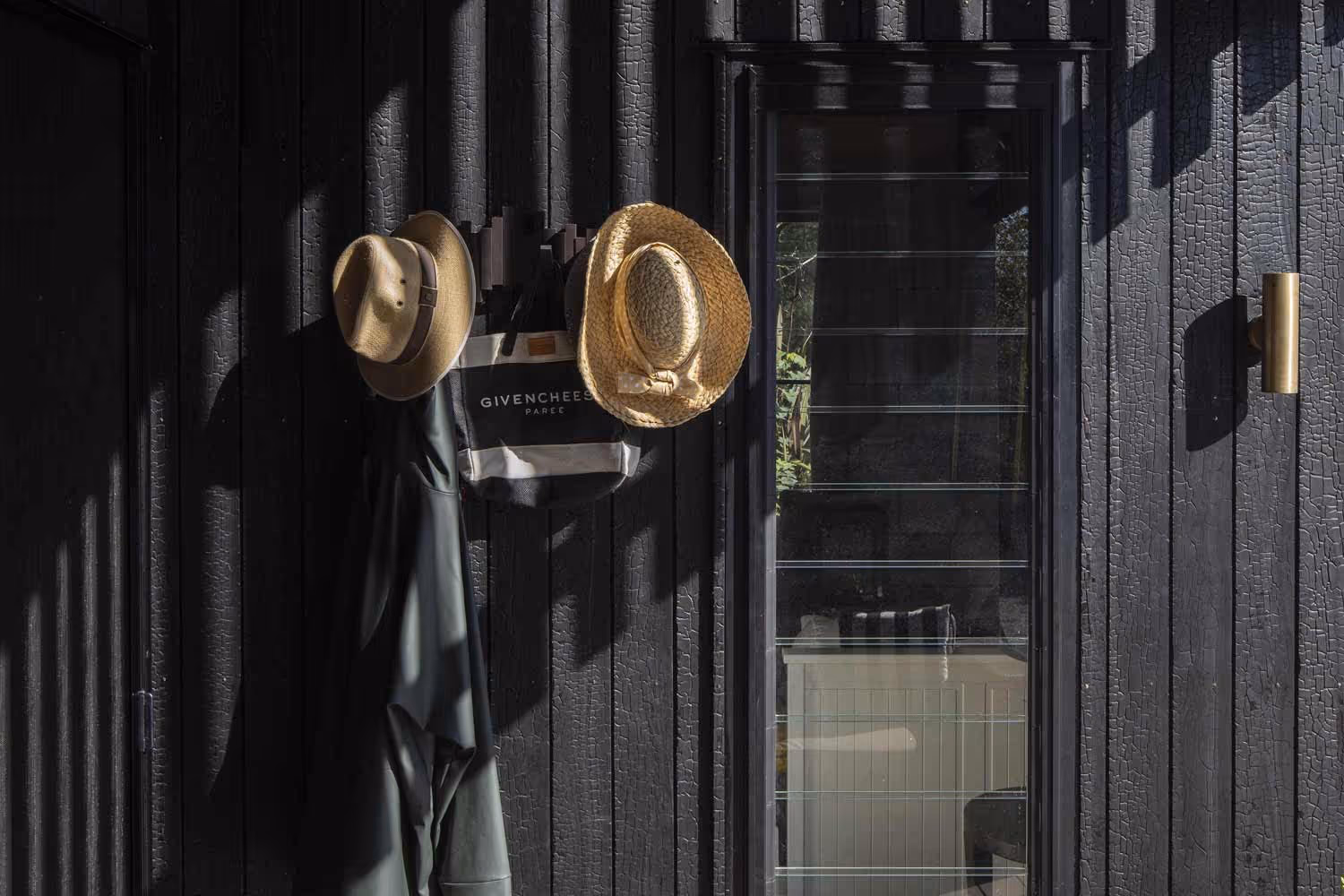 Smith House entry wall with black timber, hanging hats, coat, and tote bag.