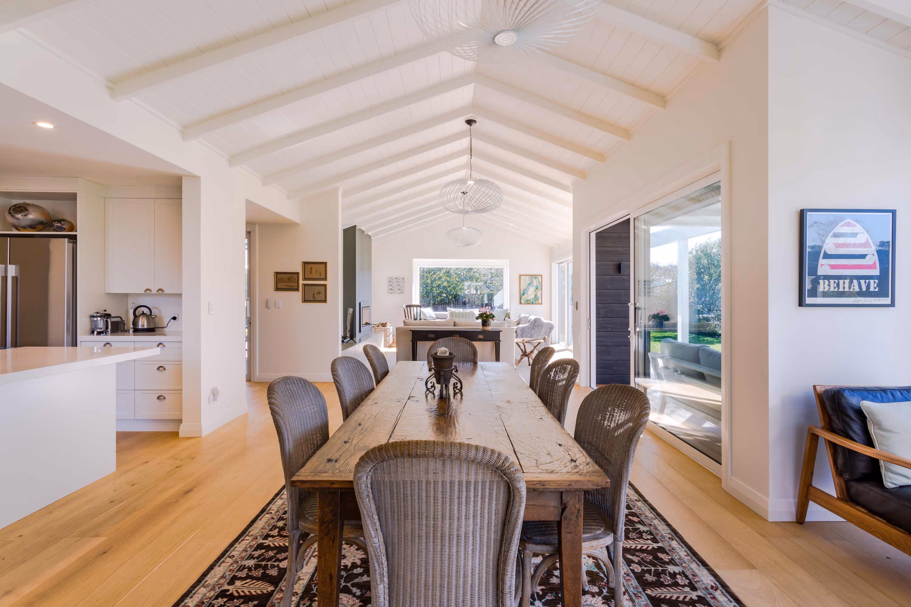 Dining area at the Kemp House in Greytown with rustic wooden table, wicker chairs, and vaulted white ceiling with pendant lights.