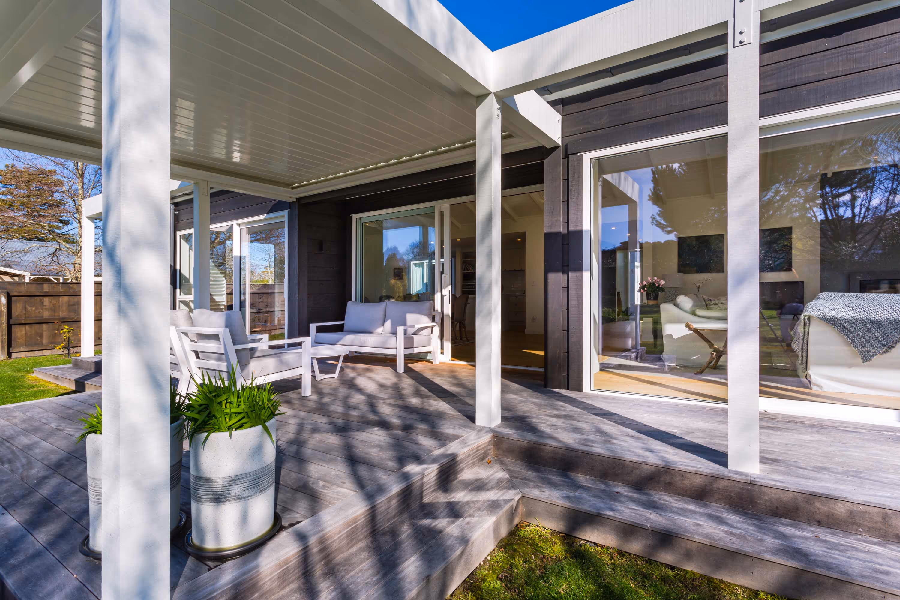 Outdoor patio at the Kemp House in Greytown with timber decking, white furniture, potted plants, and sliding glass doors to living room.