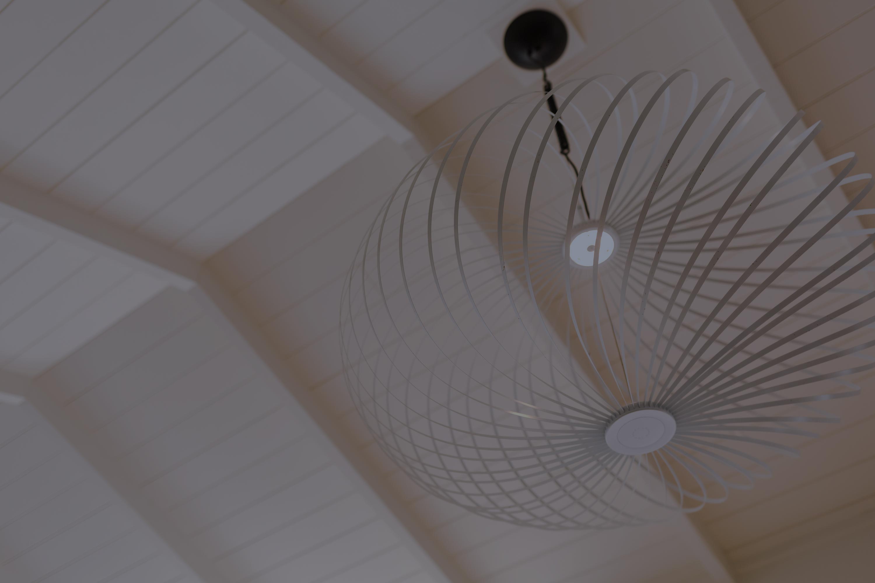 White modern ceiling light with a circular, cage-like design mounted on a white wooden ceiling.