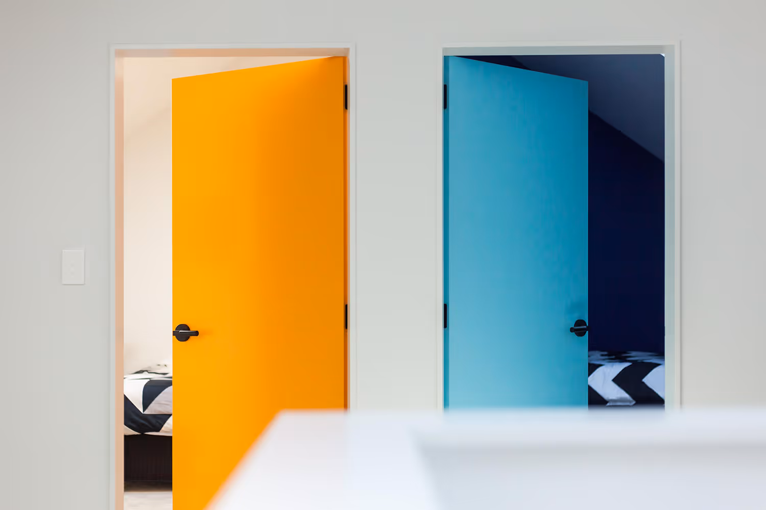 Two interior doors at the Saunders Residence in Greytown, one orange and one blue, partially open to bedrooms with patterned bedding.