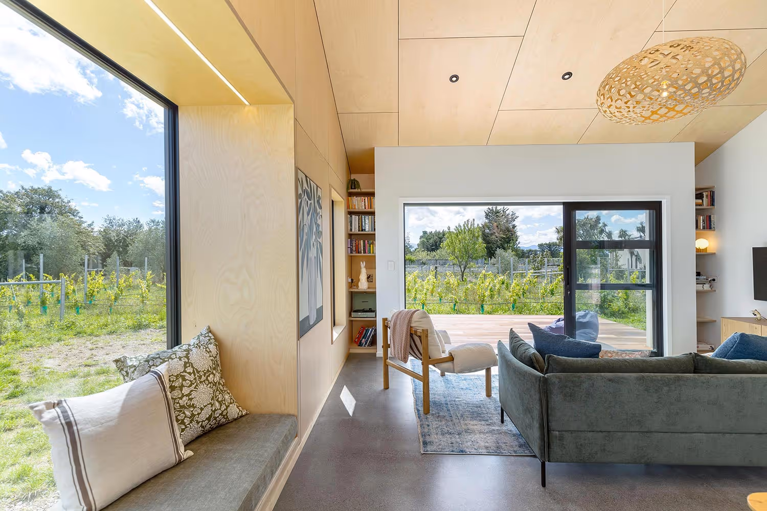 Fisher & Clarke house living room with grey sofa, armchair, bench, and vineyard views.