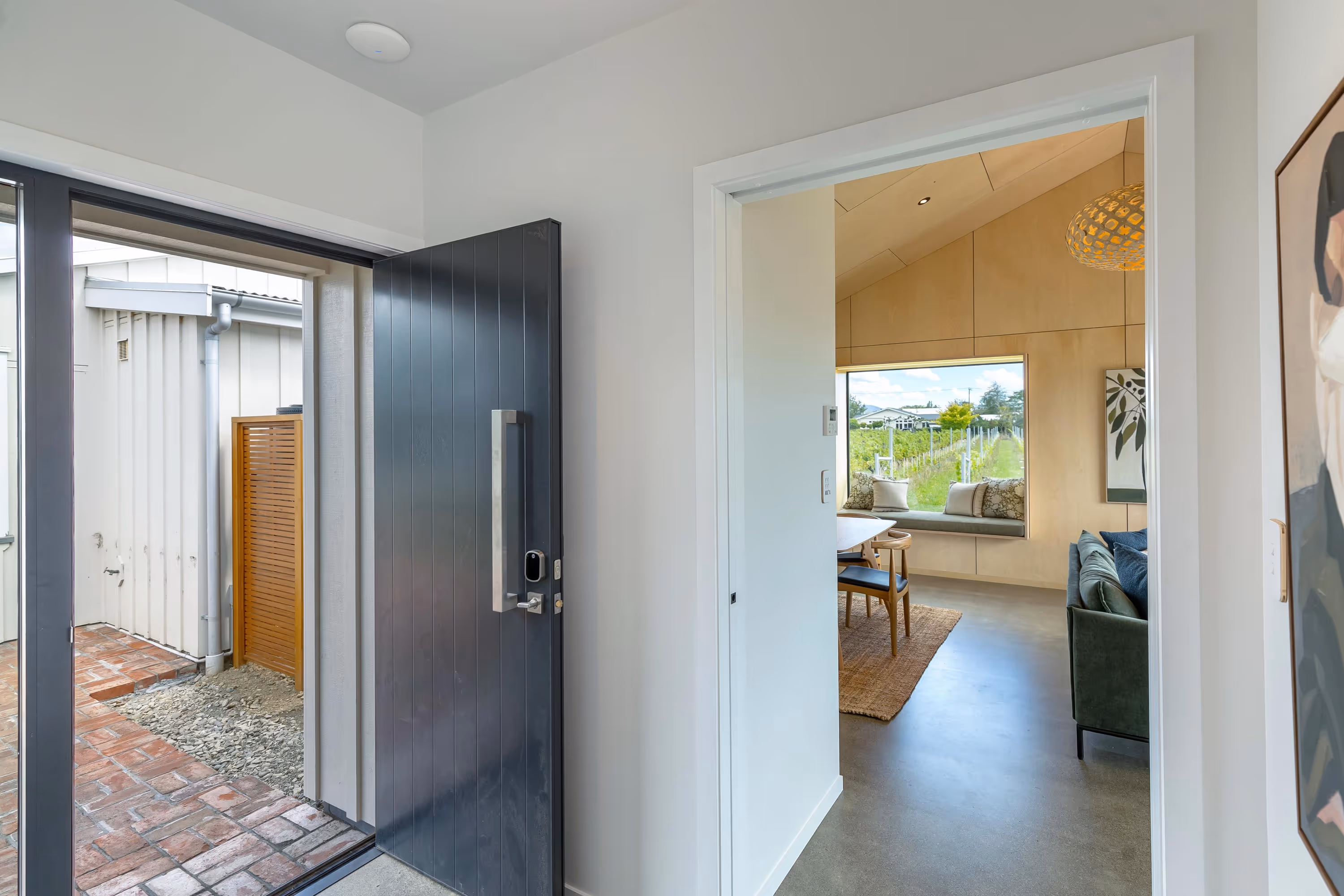 Fisher & Clarke house, front door opening to living room with green sofa, wooden chairs, and garden view.
