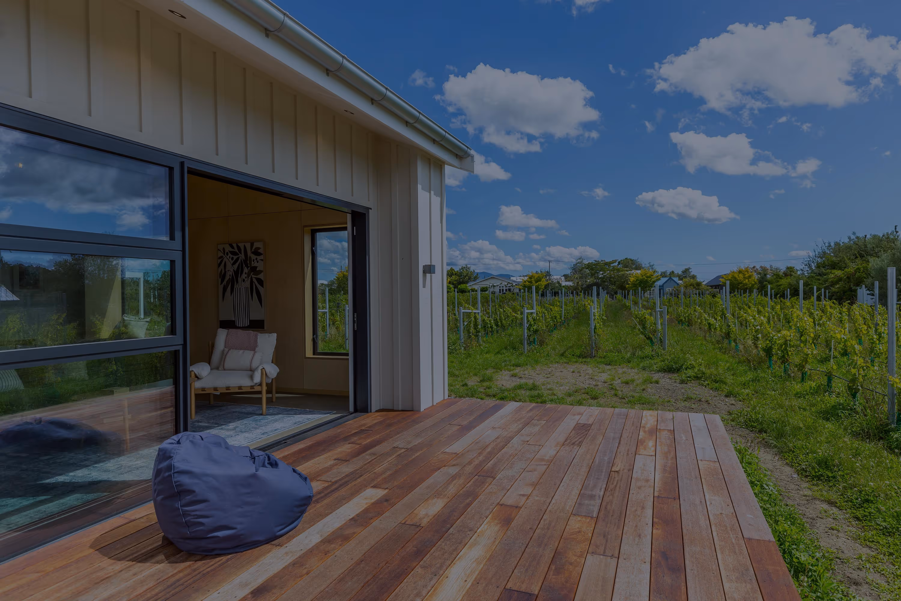 Wooden deck at Fisher & Clarke house, Martinborough with a blue bean bag and views of the vineyard under a clear sky.